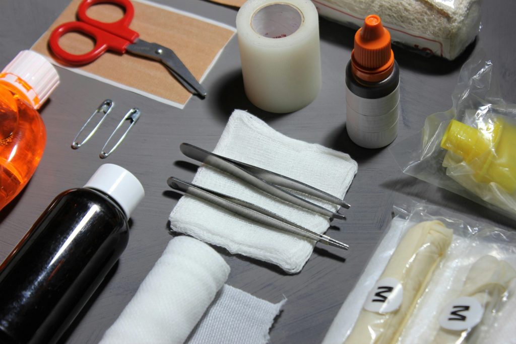 A flat lay of various first aid items including scissors, bandages, tweezers, and liquid medicines.