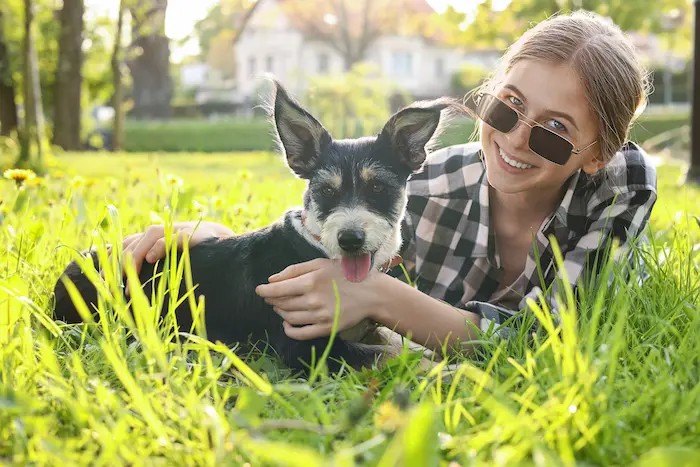 Teenage girl with her cute dog resting on green grass
